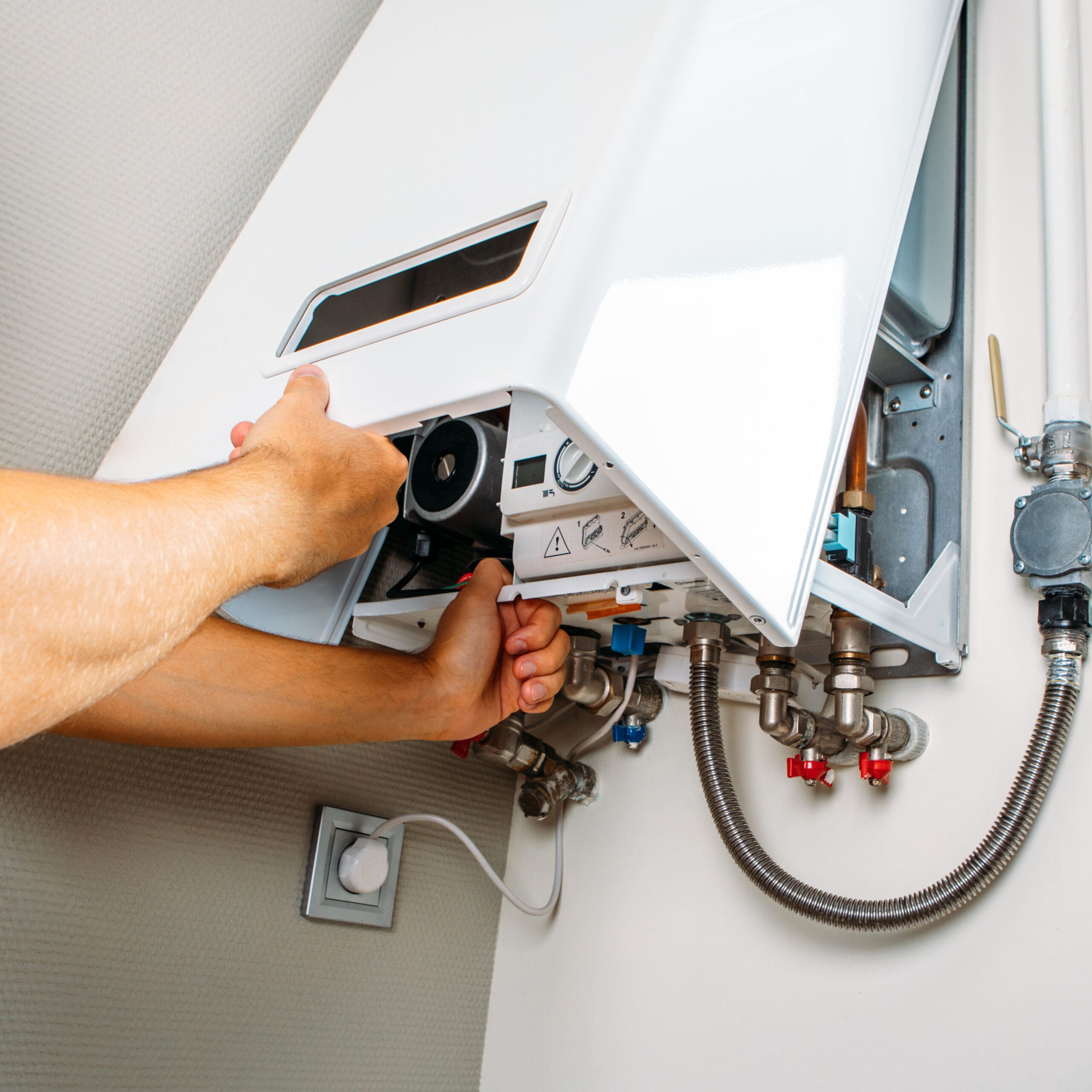 A person adjusts the settings on a wall-mounted combi boiler with the front panel open. The image shows the internal components of the boiler, including pipes and valves. The person uses both hands to manipulate the controls inside the unit.