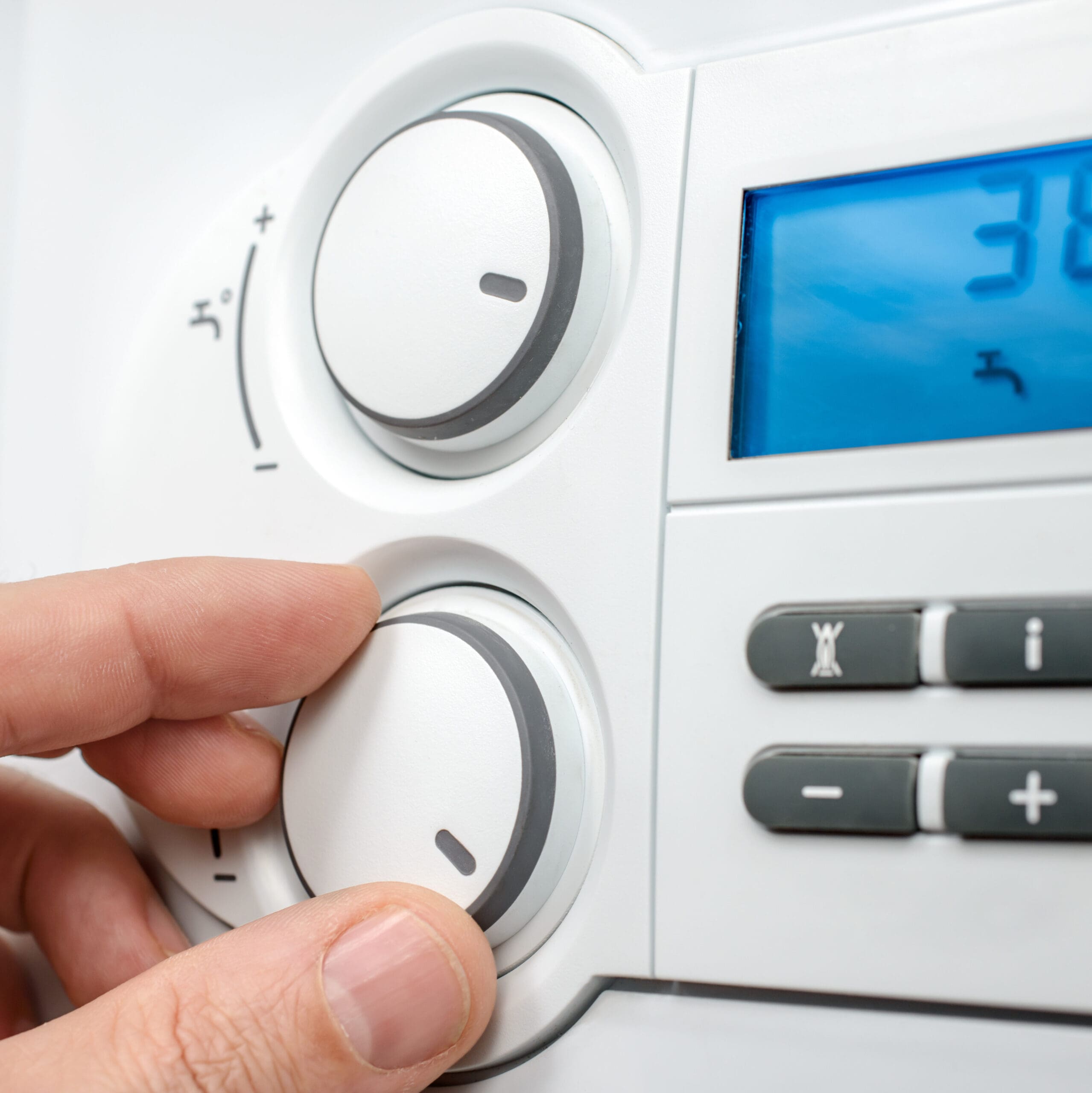 A close-up of a person's hand adjusting the temperature dial on a white digital thermostat. The device has a small blue screen displaying the number 38. There are additional buttons and controls visible next to the display.